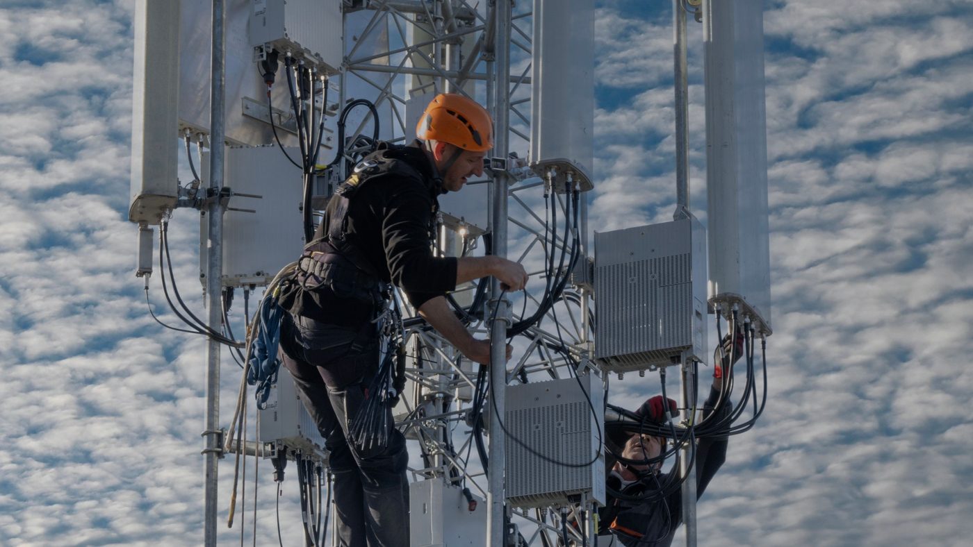 Two technicians working on a telecom tower, seen from below